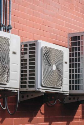 Air conditioner compressor installed on the wall of a building, along with industrial air conditioning units and ventilation systems. Cooling systems.