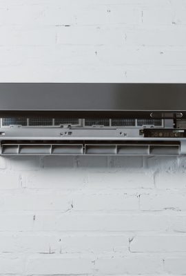 modern air conditioner with opened front plate hanging on white brick wall