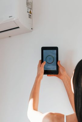 Rear view of woman that standing indoors with phone and controlling smart house technology.