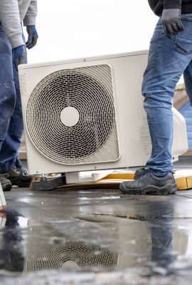 Two workers installing an air conditioning unit on a rooftop on a cloudy day.